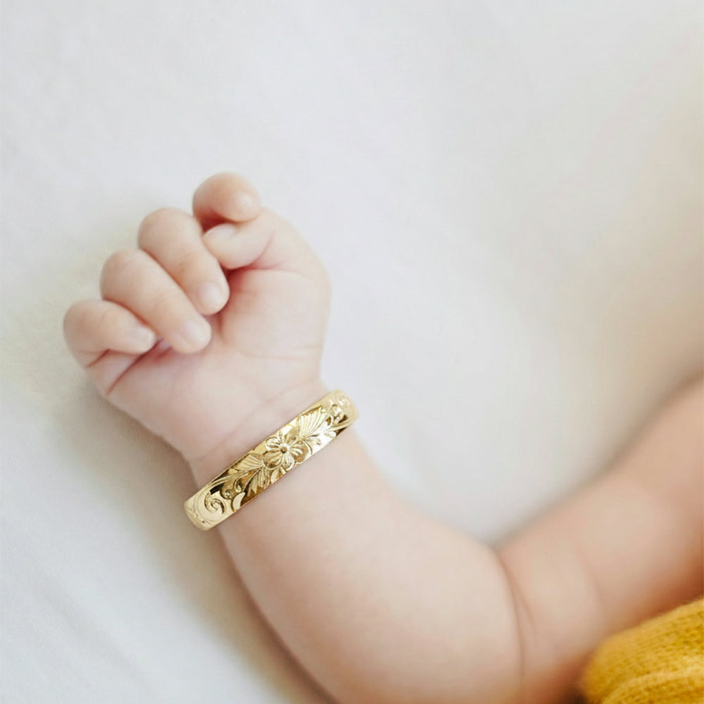 ゴールドのベビーバングルブレスレットを着けた赤ちゃんの腕