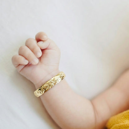 ゴールドのベビーバングルブレスレットを着けた赤ちゃんの腕